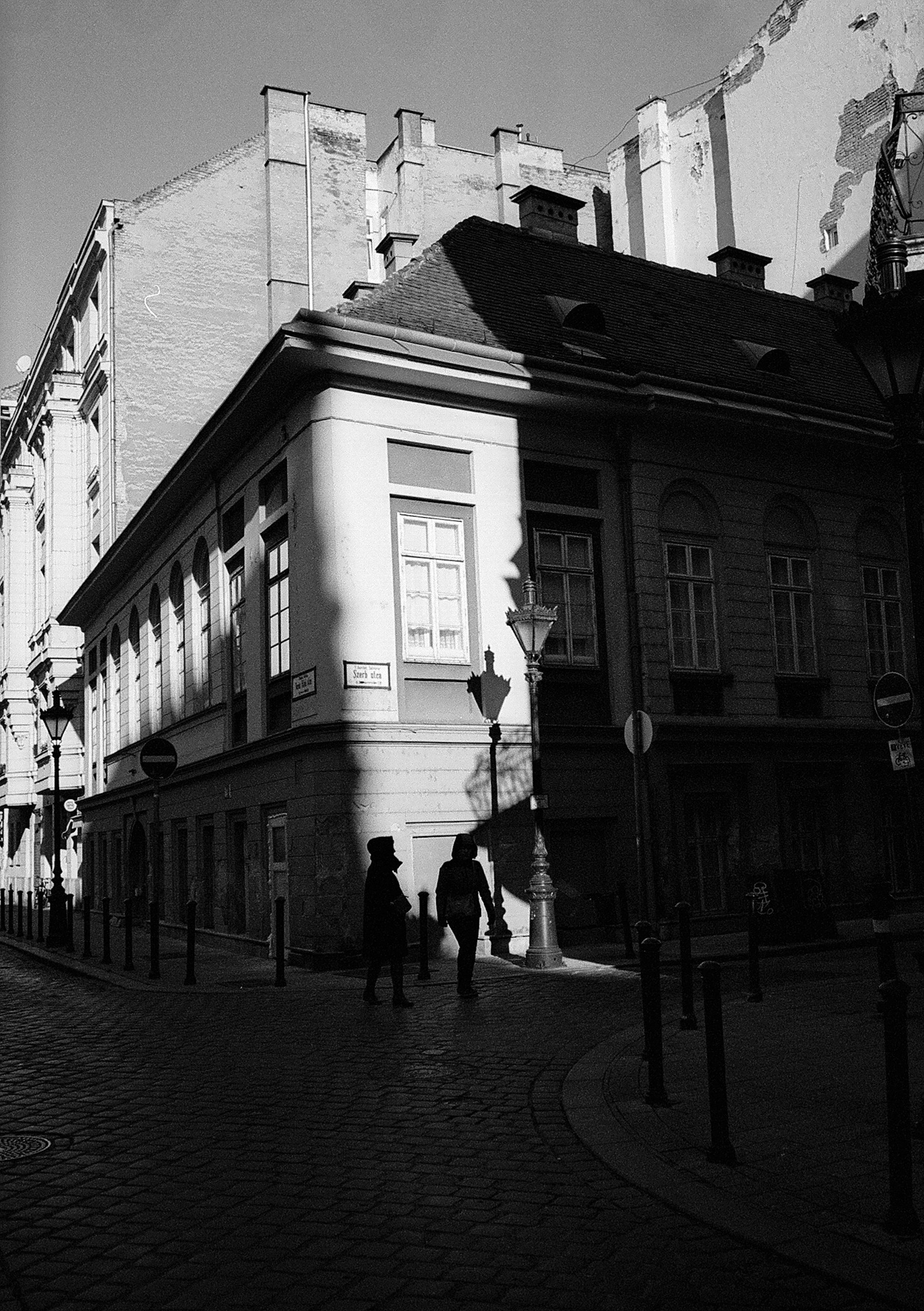 People walking through hard light and shadow on a Budapest street